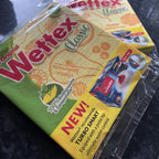 Two packs of Wettex Classic Dishcloths from Sweden on a dark countertop with a sink in the background.