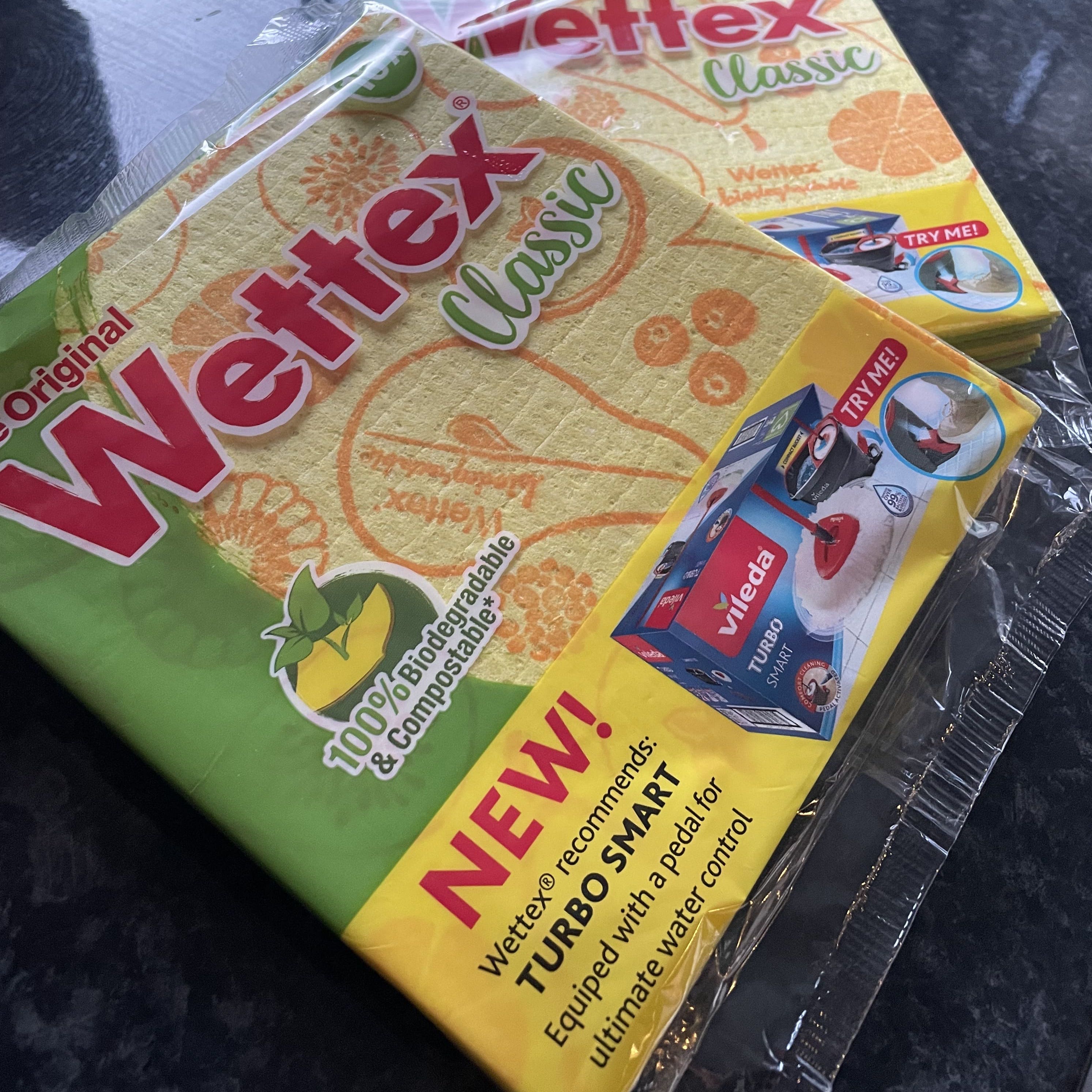 Two packs of Wettex Classic Dishcloths from Sweden on a dark countertop with a sink in the background.